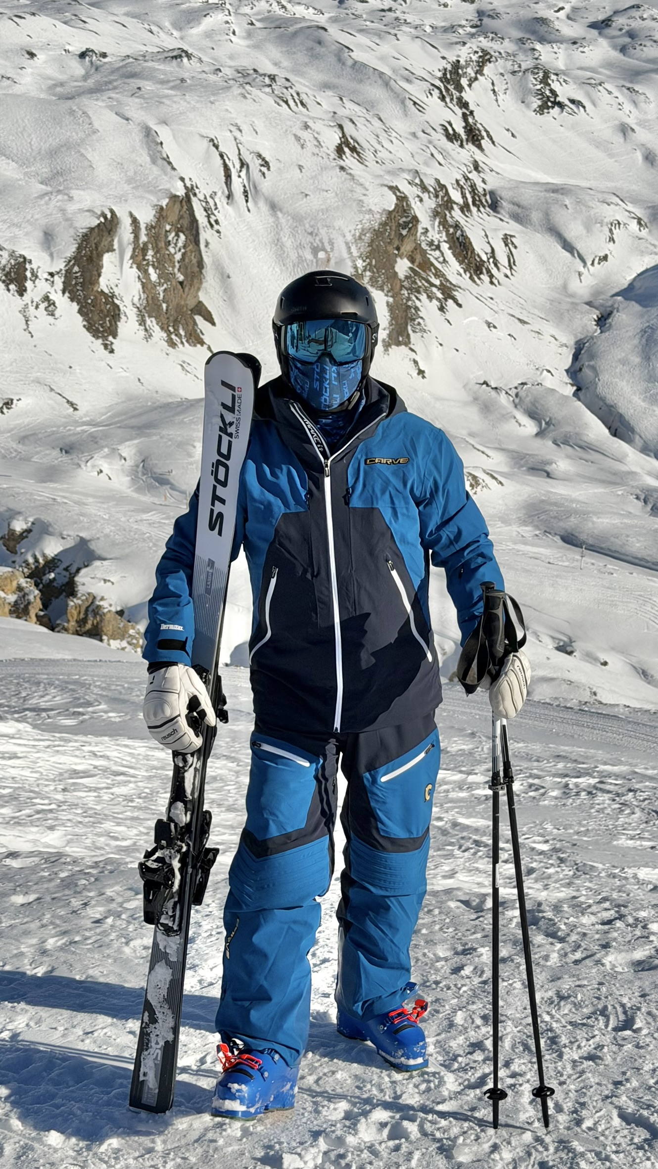 Adam in his blue CarveSport suit holding his Stöckli skis